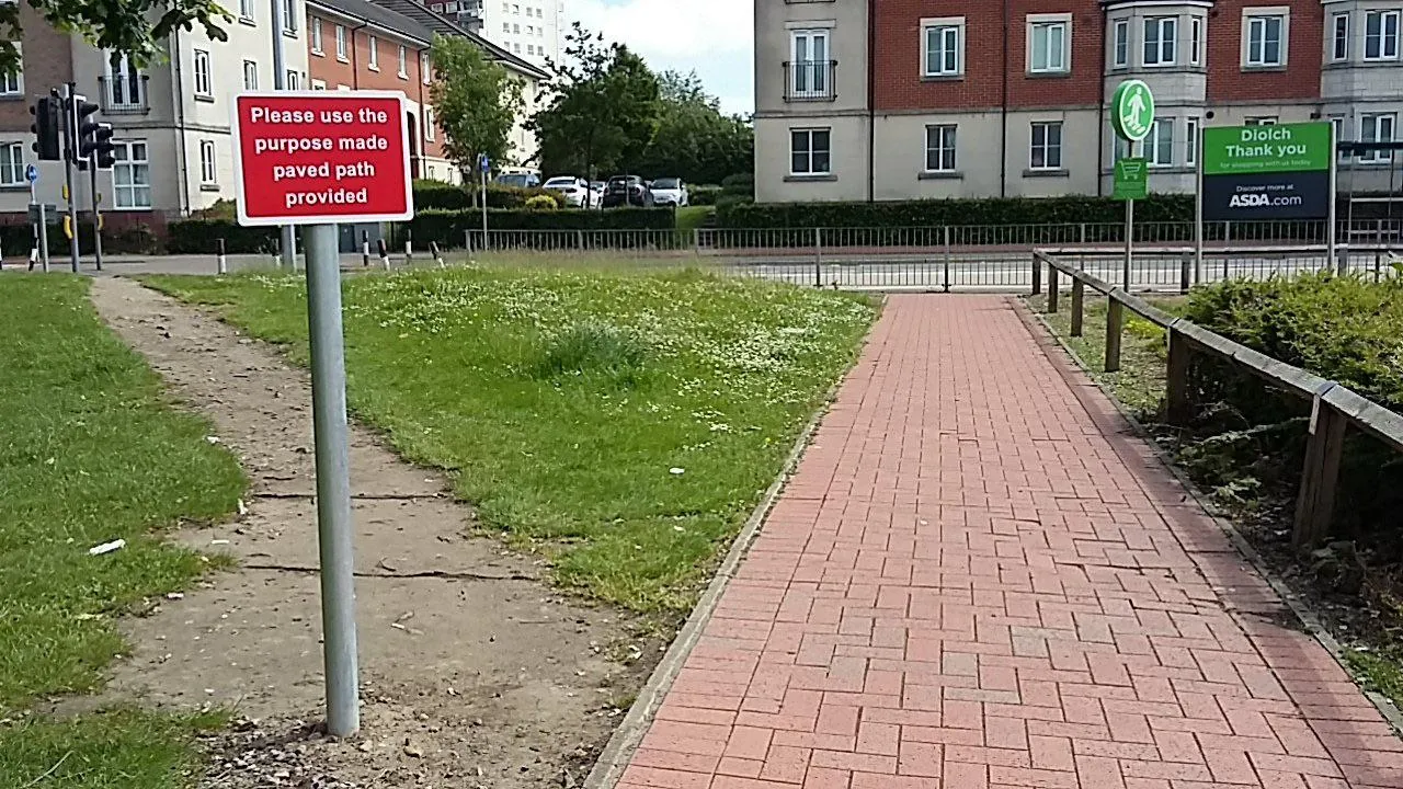 Een geplaveid pad naast een uitgesleten spoor door het gras